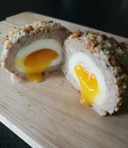 Homemade Scotch Eggs - On a chopping board, sliced in half with the middle oozing out