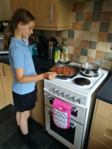 Feeding The Small Humans - Young girl standing at a cooker stirring a pan of meatballs in sauce