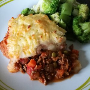 Cottage Pie - A plate with a heap of cottage pie and some green veggies next to it.