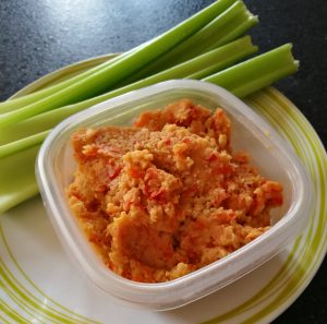 Roasted Red Pepper Hummus - A pot containing hummus with some celery sticks on the side