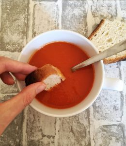 Tomato Pepper & Chorizo Soup with a piece of bread being dipped into it.