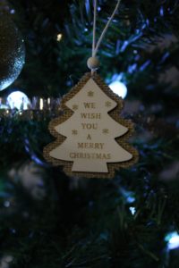 Things I Don't Like About Christmas - A white and burlap tree shaped decoration with We wish you a Merry Christmas printed on it