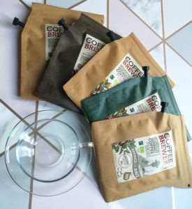 Growers Cup Review - 5 coffee bags fanned out around a glass cup on a pink and grey, geometric background 