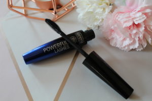 Lavera Natural Makeup - a black fading to blue mascara tube with the wand resting on top. It's sat on a geometric background with a copper candle holder and 2 flowers in the background