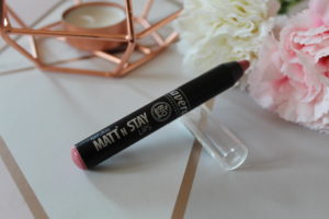 Lavera Natural Makeup - a black lip crayon with a pink end, resting on a clear lid and sat on a geometric background with a copper candle holder and flowers on the background