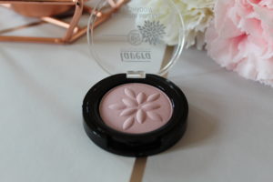 Lavera Natural Makeup - A single eyeshadow pot with it's lid open in a pale lilac colour sat on a grey and gold background