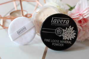 Lavera Natural Makeup - A black lid, the open pot of powder and a powder applicator stood on their side against copper candle holder and flowers