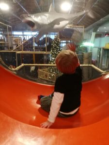 Soft Play Mum Guilt - Toddler sat in an orange and plastic bubble overlooking soft play equipment