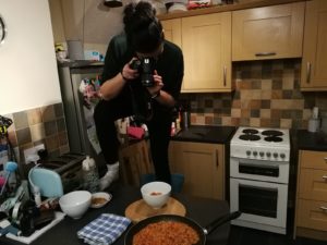 Living With A Blogger - Carly half standing on a kitchen counter with a DSLR taking pictures from above of a bowl and a pan of food.