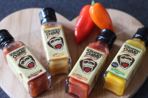 Screaming Chimp - 4 sauce bottles lying on a heart shaped wooden board with 2 small peppers above them.