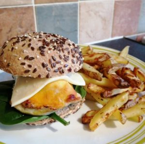 Screaming Chimp - A yellowish chicken breast in a seeded bun with some lettuce on the bottom and a slice of plastic cheese on top of the chicken. A portion of fries is next to the burger. 