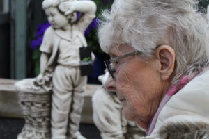 Loneliness in the elderly - a close up picture of an elderly lady's face with a statue of a boy in the background 