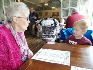 Loneliness in the elderly - An elderly lady sat at a table talking to a toddler boy.