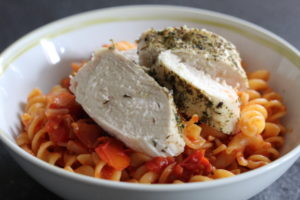 Herby Chicken with Sundried Tomato Pasta - a bowl of red pasta with clices of chicken laying on top