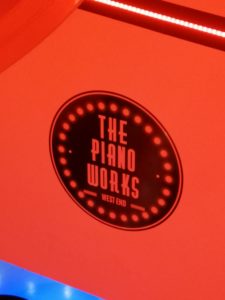 The Piano Works logo written in black on a bright red wall