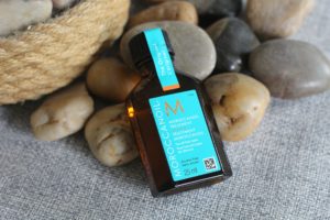 July 19 Glossybox - a brown bottle of hair oil with a turquoise label laying on rocks