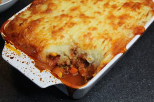 Cottage Pie - A white dish with splatters all over the sides filled with cottage pie but a spoonful has already gone