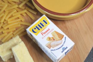 Cheats MAc and Cheese - Carton of CHEF cooking cream laying on a chopping board surrounded by dry macaroni,blocks of cheese and a terracotta dish