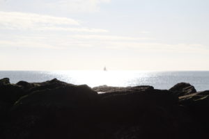 New Year Revelation - a small boat centrerd in the sunlight on the sea with rocks silhouetted in front. 