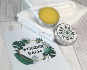 Wonder Balm - 2 white face cloths with the open tin of balm sat on top. Next to it is a card with Wonder Balm and leaves circling the words