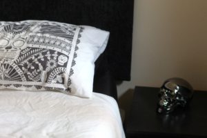 How to get a better night's sleep - white bedsheets and pillows against a black headboard with a black side-table and a black metallic skull sat on it.