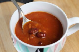 Mexican Chilli Bean Soup - A large mug type bowl filled with a red/brown coloured soup and a silver spoon lifting some beans out of it