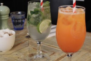 5 New Things To Learn - a couple of cocktail looking drinks on a wooden table. 1 looks like a mojito and the other a tequila sunrise.