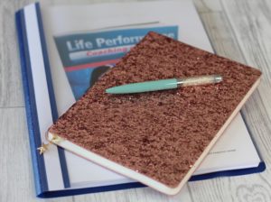 5 New Things To Learn - A Glittery notebook on top on top of a plastic fronted folder with learning material inside. A tiffany blue pen rests on top of the notebook.