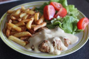 Gluten Free IKEA Style Meatballs covered with sauce on a plate with chips and salad