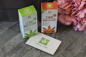 2 boxes, one green and white and the other brown and white stood up with a business card under the corner of one with Herts Hemp and a cannabis leaf logo on it