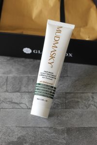 A white tube with gold branding leaning against the Glossybox box