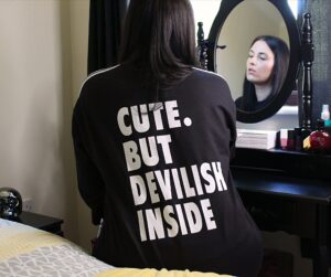 Carly sat at a black dressing table with her back to the camera and you can see her reflection in the mirror. She's wearing the black and white tracksuit that has the words "cute but devilish inside" on it in white letters.