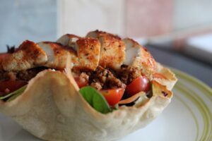 Taco Salad Bowl - A wrap in a bowl shape holding salad, riced veg and sliced chicken on top