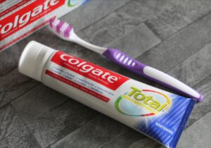 A tube of toothpaste lying next to a purple and white toothbrush