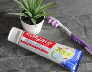 Fun ways of getting kids to look after their teeth - A tbe of Colgate toothpaste lying on a grey tiled background next to a purple and white toothbrush and a small potted plant