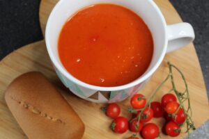 simple tomato and basil soup in a bowl with tomatoes and a bread roll next to it