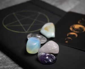 What is Wicca? Some different crystals placed on top of a black notebook with a gold pentagram symbol on it.